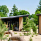 Moderne tiny house med træfacade kaldet Sand Lodge i Holiday Park De IJsvogel, omgivet af sand og grønne træer.