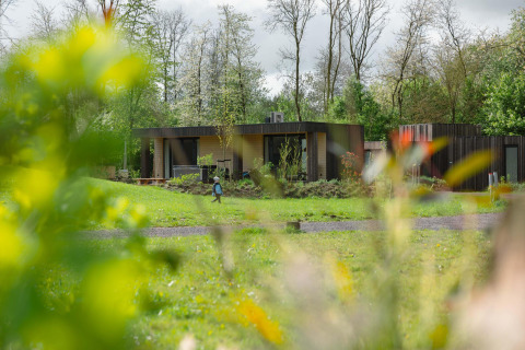Lodge Jacuzzi im Resort de Parel in den Niederlanden, eingebettet im Grünen, mit Bäumen und einer Person im Garten.