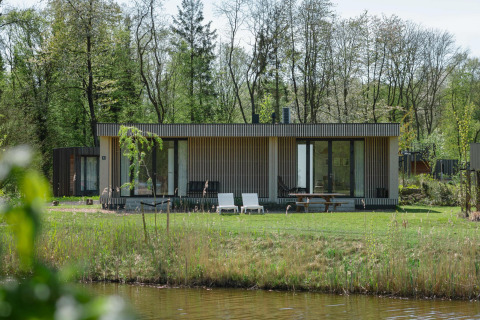 Lodge moderno con facciata in legno e ampie vetrate, immerso nel verde vicino a un laghetto in primavera.