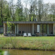 Lodge moderno con fachada de madera y ventanales grandes, rodeado de naturaleza y junto a un estanque.