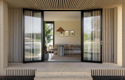 Entrada abierta a un lodge moderno con paneles de madera, puertas de vidrio grandes y decoración minimalista.
