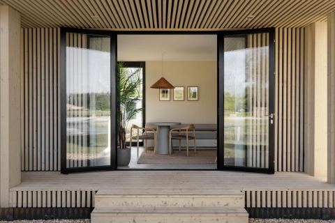 Åben indgang til en moderne lodge med træbeklædning, store glasdøre og minimalistisk interiør.
