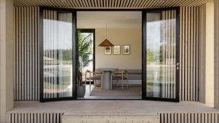 Open entree van een moderne lodge met houten bekleding, grote glazen deuren en een minimalistisch interieur.