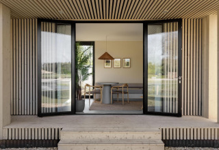 Åben indgang til en moderne lodge med træbeklædning, store glasdøre og minimalistisk interiør.