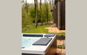Outdoor hot tub on a wooden deck at a lodge, surrounded by green trees and nature in the springtime.