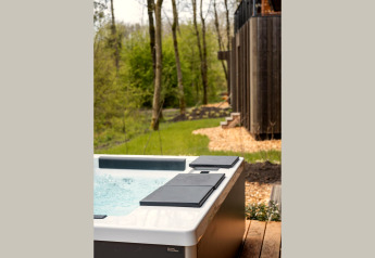Whirlpool auf einer Holzterrasse bei einer Lodge im Wald, umgeben von frischem Grün im Frühling.