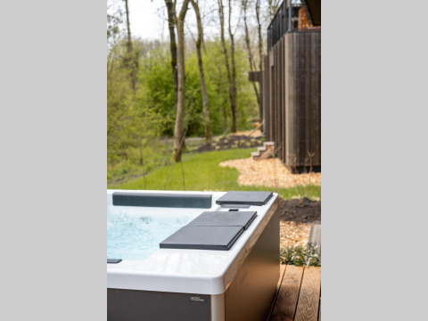 Bain à remous extérieur sur terrasse en bois près d’un lodge, entouré d’arbres verts et de nature.