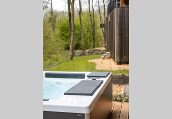 Jacuzzi exterior sobre una tarima de madera junto a una cabaña, rodeado de árboles y naturaleza verde.