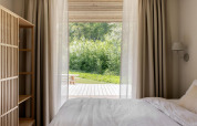 Camera accogliente in una lodge con tende chiare, letto morbido e vista su terrazza e verde esterno.