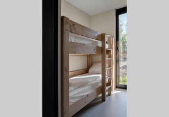 Chambre de lodge avec lit superposé en bois, draps blancs et grande fenêtre donnant sur la nature.