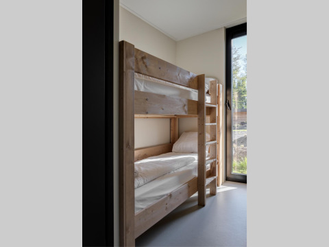 Habitación en un lodge con litera de madera, ropa de cama blanca y gran ventana con vistas al exterior natural.