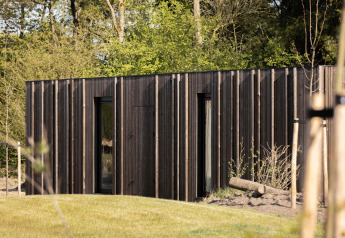Pavillon moderne en bois avec lames verticales, entouré de verdure et d’un paysage forestier naturel.
