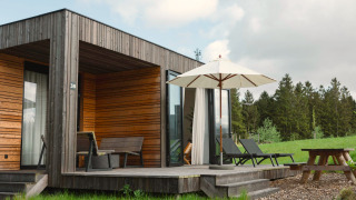 Modern wooden villa with sun loungers, umbrella, and picnic table at Resort de Parel in the Netherlands.