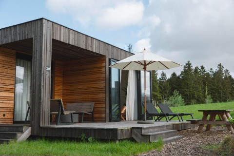 Villa moderna de madera con tumbonas, sombrilla y mesa de picnic en Resort de Parel, rodeada de naturaleza.