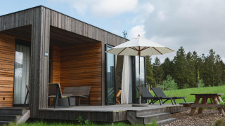 Moderne Holzvilla mit Terrasse, Liegestühlen und Sonnenschirm im Resort de Parel, umgeben von Natur.