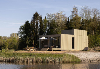 Moderne lodge ved søen omgivet af træer på Resort de Parel i Holland, set i morgensolen.