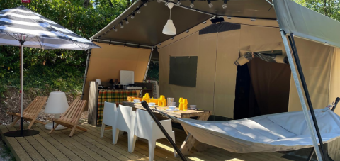 Udendørsområde ved luksustelt Base Lodge på Camping Gajole i Italien med spisebord, liggestole og hængekøje.
