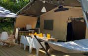Área exterior de la Base Lodge en Camping Gajole, Italia, con comedor, sillas, hamaca y sombrilla.