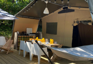 Área exterior de la Base Lodge en Camping Gajole, Italia, con comedor, sillas, hamaca y sombrilla.