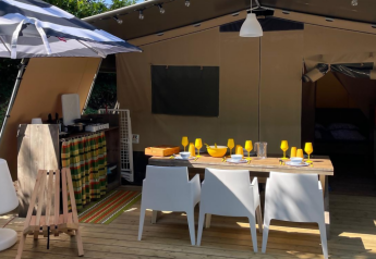 Safari Base Lodge op Camping Gajole in Italië met open tent, eetplek, buitenkeuken en grote parasol.