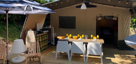Safari Base Lodge at Camping Gajole, Italy, featuring an open tent setup with dining area, kitchen, and umbrella.