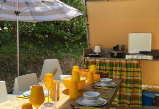 Área de comedor y cocina al aire libre en la tienda safari Base Lodge en Camping Gajole, Italia, con parasol.