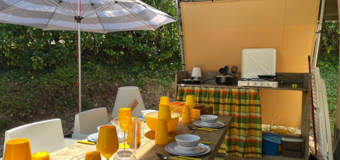 Outdoor dining area and kitchen in Base Lodge safari tent at Camping Gajole, Italy, under a parasol.