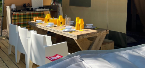 Mesa de madera con vasos amarillos en tienda safari en Base Lodge, Camping Gajole, Italia.