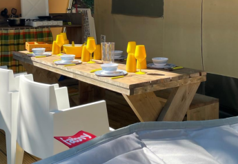 Mesa de madera con vasos amarillos en tienda safari en Base Lodge, Camping Gajole, Italia.