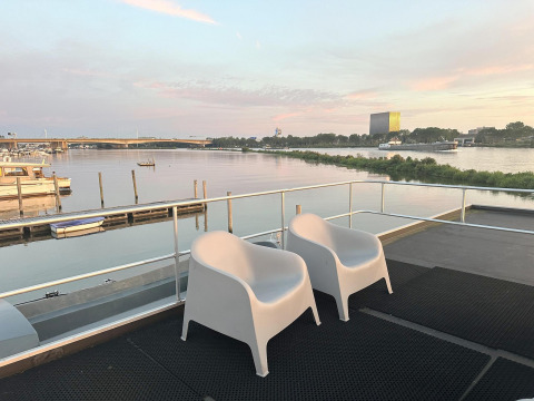 Two white chairs on the deck of a houseboat at Marina Parcs Amsterdam overlooking calm water at sunset.