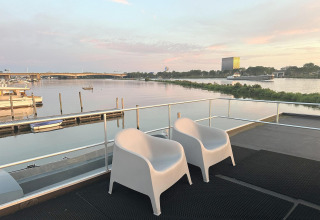 To hvide stole på dækket af en husbåd i Marina Parcs Amsterdam med udsigt over vandet ved solnedgang.