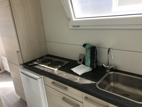 Compact kitchenette with stovetop, sink, and large window inside Havenlodge+ houseboat at Marina Parcs Amsterdam.