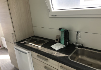 Compact kitchenette with stovetop, sink, and large window inside Havenlodge+ houseboat at Marina Parcs Amsterdam.