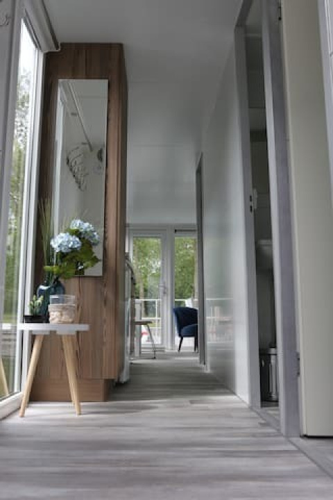 Pasillo moderno en una casa flotante con ventanales, mesa con flores y terraza en Havenlodge+ Ámsterdam.