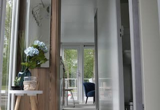 Moderne gang på en husbåd med store vinduer, blomsterbord og kig til terrasse hos Havenlodge+ Amsterdam.