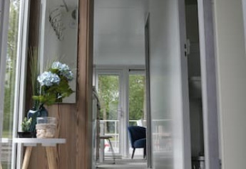 Moderne gang på en husbåd med store vinduer, blomsterbord og kig til terrasse hos Havenlodge+ Amsterdam.