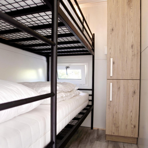 Moderne woonbootkamer met metalen stapelbed, houten kledingkast en klein raam voor daglicht.
