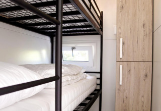 Habitación de casa flotante moderna con literas metálicas, armario de madera y pequeña ventana lateral.