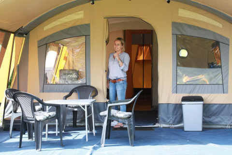 Kvinde står foran en safaritelte på CharmeCamping De Regge-Vallei i Holland med plastikmøbler.