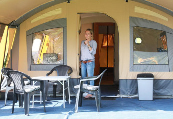Donna davanti a una tenda safari al CharmeCamping De Regge-Vallei nei Paesi Bassi, con sedie di plastica.