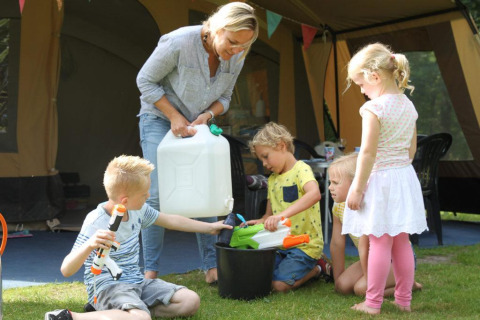 Een vrouw en vier kinderen spelen met waterpistolen buiten bij een safaritent op CharmeCamping De Regge-Vallei.