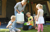 Een vrouw en vier kinderen spelen met waterpistolen buiten bij een safaritent op CharmeCamping De Regge-Vallei.