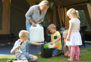 Eine Frau und vier Kinder spielen draußen an einem Safarizelt bei CharmeCamping De Regge-Vallei mit Wasserpistolen.