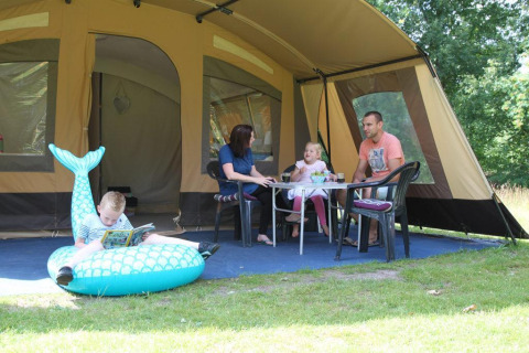 Familie hygger sig foran en safaritelte på CharmeCamping De Regge-Vallei i Holland, med børnene leger.