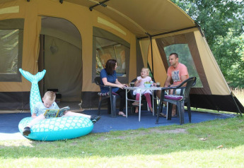 Familie hygger sig foran en safaritelte på CharmeCamping De Regge-Vallei i Holland, med børnene leger.
