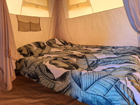 Interno di una tenda safari al CharmeCamping De Regge-Vallei nei Paesi Bassi con letto a fantasia foglie.
