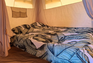 Interior of a safari tent at CharmeCamping De Regge-Vallei in the Netherlands with a leafy-patterned bedspread.
