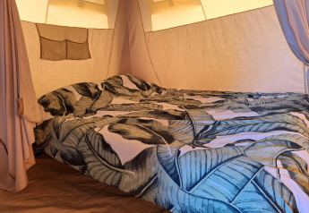 Innenaufnahme eines Safari-Zeltes mit gemütlichem Bett und Blätter-Bettwäsche auf Campingplatz De Regge-Vallei.