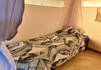 Lit simple avec draps à motif de feuilles dans une tente safari au CharmeCamping De Regge-Vallei, Pays-Bas.