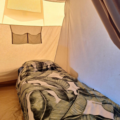 Vista interior de dormitorio en tienda safari con cama individual y edredón de hojas en los Países Bajos.